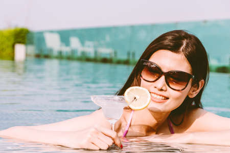 Woman wearing bikini drinking cocktail in swimming pool on summer vacation relaxing at resort spaの写真素材