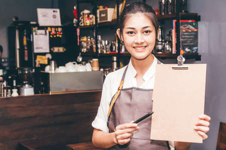 Barista holding Menu in front of counter bar in coffee shop restaurantの写真素材