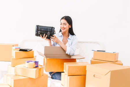Young woman freelancer working sme business online shopping and packing woman bag with cardboard box on bed at home - Business online shipping and delivery conceptの写真素材