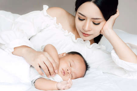 Mother holding sleeping baby hand on white bed.Love of family conceptの写真素材