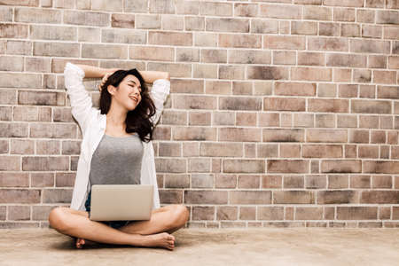 Portrait of fashion young beautiful woman model use laptop computer on copy space brick wall backgroundの写真素材