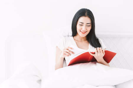 Woman reading book on bed in the morningの写真素材