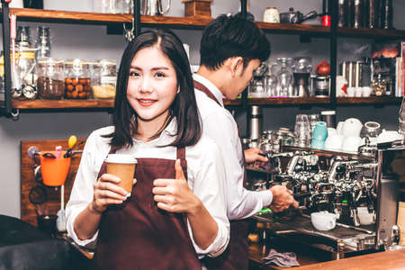 Woman barista giving coffee cup to customer at cafeの写真素材