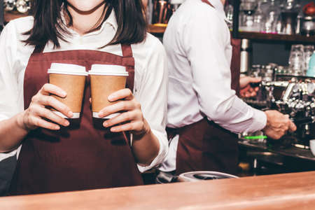 Woman barista giving coffee cup to customer at cafeの写真素材