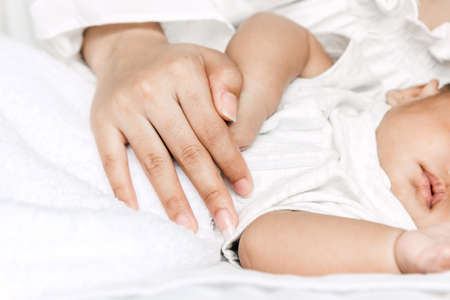 Mother holding sleeping baby hand on white bed.Love of family concept