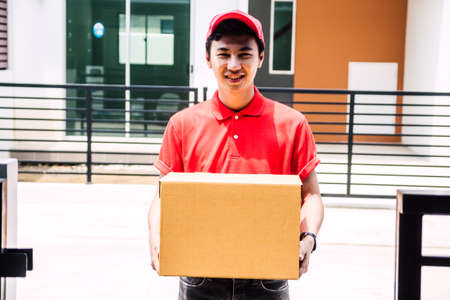 Delivery man with cardboard  box near house of customerの写真素材