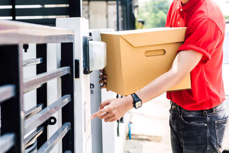 Delivery man with cardboard  box near house of customerの写真素材