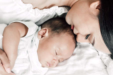 Mother holding baby in her arms and kiss in a white bedroom.Love of family concept