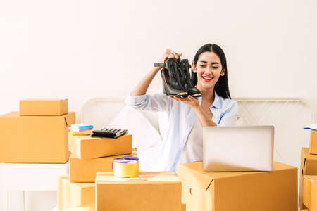Young woman freelancer working sme business online shopping and packing shoes with cardboard box on...