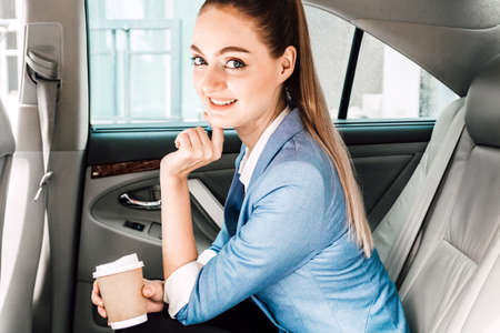 Businesswoman holding cup of coffee in back seat of luxury car