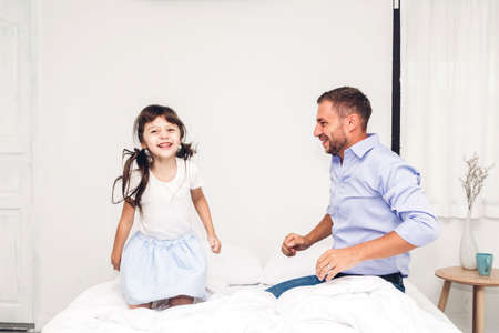 Father with little daughter having fun and playing together on the bed at home.Love of family and father day conceptの写真素材