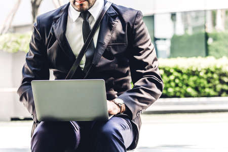 Handsome businessman in black elegant suit sitting and working with laptop computer on the city.Business and startup idea conceptの写真素材