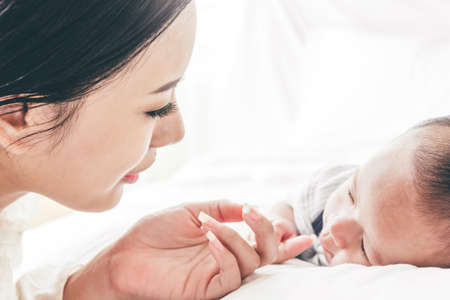 Mother holding sleeping baby hand on white bed.Love of family concept
