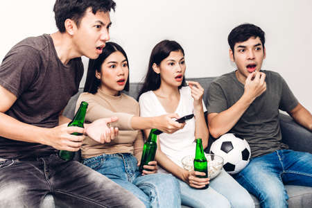 Group of friends eating popcorn and drinking beer together and watching soccer game on sofa at home.Friendship and party conceptの写真素材