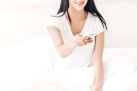 Woman holding remote air conditioner on bed in the bedroom