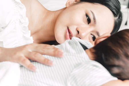 Mother holding sleeping baby hand on white bed.Love of family concept