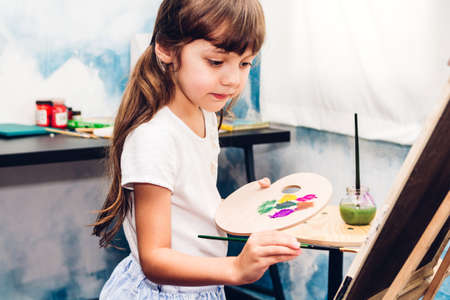 Little girl artist drawing on canvas with color palette and watercolor paints at homeの写真素材