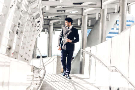 Portrait of handsome businessman in black suit standing outdoors on modern city backgroundの写真素材