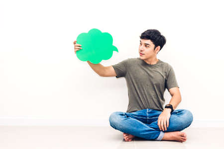 Young man sitting on floor and holding up a speech bubble icon against copy space for adding text...