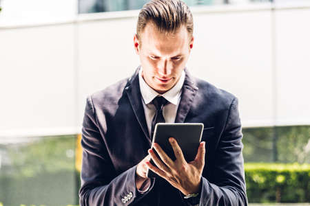Handsome businessman in black elegant suit sitting and working with tablet computer on the city.Business and technology conceptの写真素材