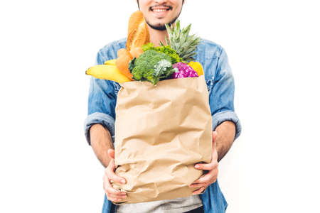 Man holding shopping paper bag with fruit and vegetables on white background