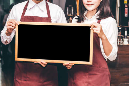 Portrait of couple barista small business owner smiling and holding empty chalkboard wooden frame in...