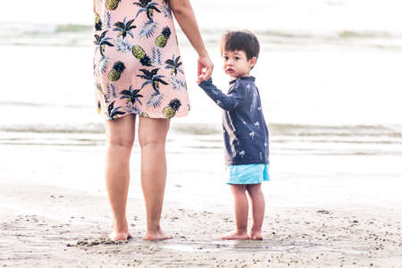 Mother and little boy holding hands standing on the beach.Love of family concept