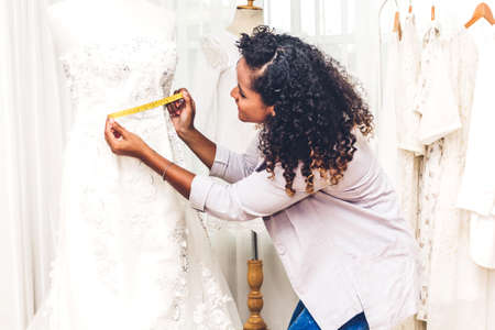 Smiling african american black woman fashion designer standing  working and using tape meter fitting on dress on the mannequin at workshop studioの写真素材