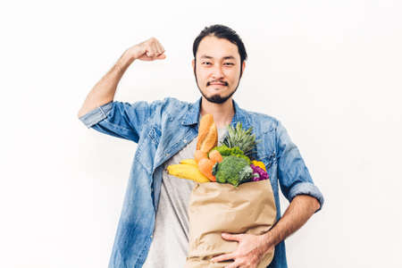 Man holding shopping paper bag with fruit and vegetables on white backgroundの写真素材