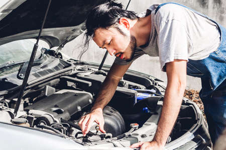 Professional car mechanic in uniform  fixing a car engine and repairing checking under the car hood...