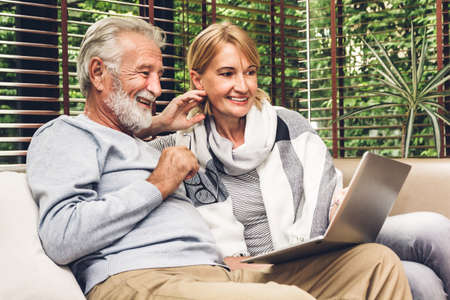 Senior couple relaxing and using laptop computer together sitting on sofa in living room at...