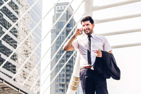 Portrait of handsome businessman in black suit standing and using smartphone outdoors on modern city background.man working with technology devices conceptの写真素材