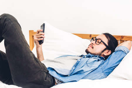 Man relaxing using and talking by smartphone on the bed at home.technology and communication conceptの写真素材