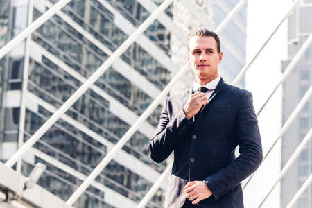 Portrait of handsome businessman in black suit standing outdoors on modern city backgroundの写真素材