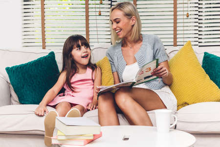 Mother with little daughter having fun and read the book together on the sofa at home.Little girl...