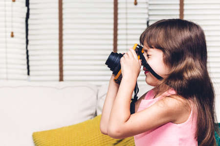 Little cute girl taking a picture with vintage camera at homeの写真素材