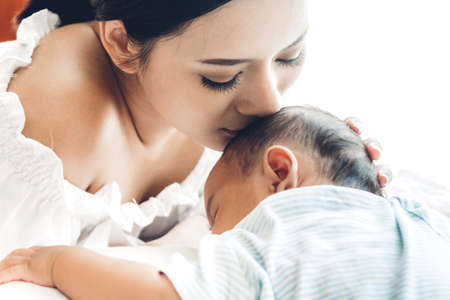 Mother kiss and holding sleeping baby hand on white bed.Love of family conceptの写真素材
