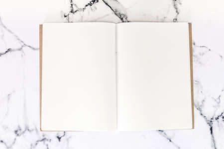 Top view of workspace and opened notebook with mock up blank pages on white marble background.Flat layの写真素材