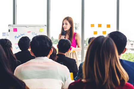 Businesswoman standing in front of group of people in consulting meeting conference seminar at hall...