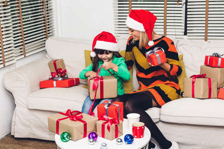 Mother and little daughter in santa hats having fun and exchanging  gifts box near christmas decoration at home.Merry Christmas and Happy new year conceptの写真素材