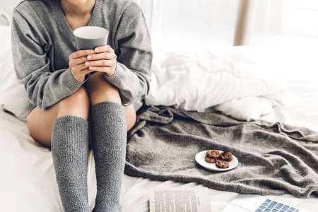 Young woman relaxing and drinking cup of hot coffee or tea on a cold winter day in the bedroom.Winter and cold weather conceptの写真素材
