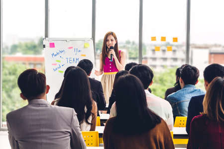 Businesswoman standing in front of group of people in consulting meeting conference seminar at hall...