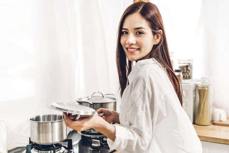 Smile woman standing and cooking by the stove and pot to prepare ingredient for cooking food in the...