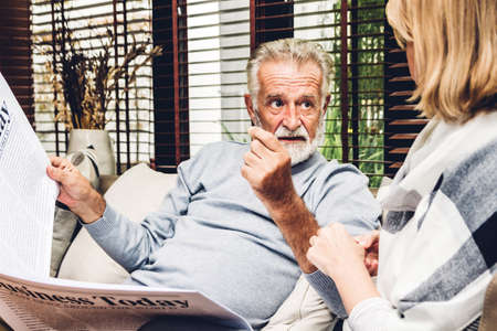 Senior couple relax talking and reading newspaper together on sofa in living room at home.Retirement couple conceptの写真素材