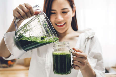 Healthy woman enjoy making green vegetables detox cleanse and green fruit smoothie with blender in kitchen at home.dieting concept.healthy lifestyleの写真素材