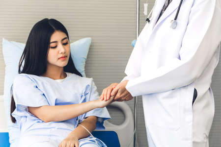 Female doctor consulting and holding hand patient reassuring with care on doctors table in...