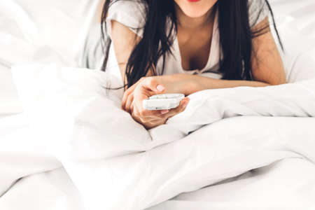 Woman holding remote air conditioner on bed in the bedroom