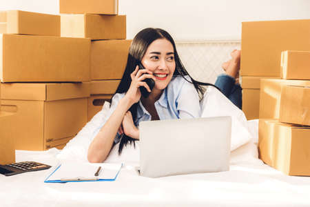 Young woman freelancer working and use laptop computer with cardboard box on bed at home - SME business online and delivery conceptの写真素材