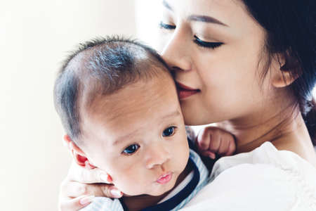 Mother holding baby in her arms and kiss in a white bedroom.Love of family concept