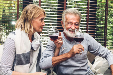 Senior couple relax talking and drinking wine glasses together on sofa in living room at home.Retirement couple conceptの写真素材